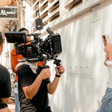 Film crew shooting a scene with professional video camera and actress outdoors on a sunny day.