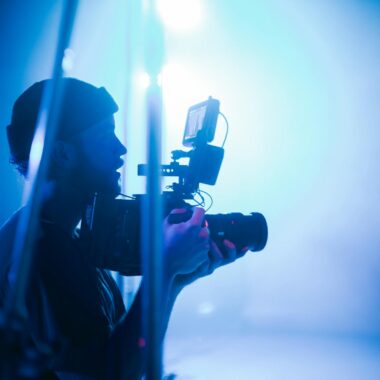 Silhouette of a cinematographer using camera equipment in a vibrant blue-lit studio.